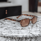 X-KD's 100 zonnebril met schildpadmontuur en amberkleurige glazen op een wit marmeren werkblad.